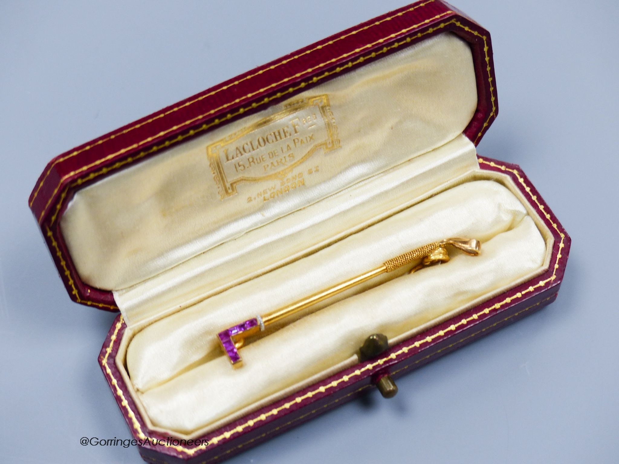 A Lacloche Freres gold and ruby riding whip brooch, signed, gross 3g, 5cm. In original box.